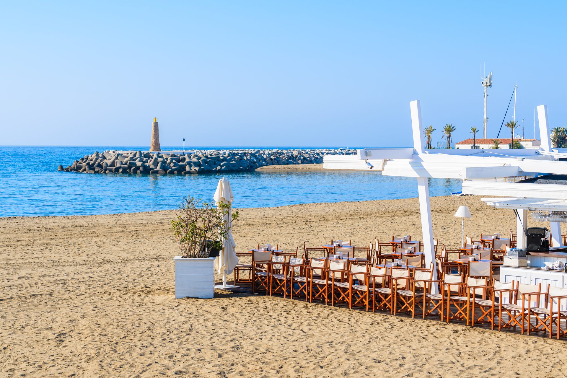 Beachfront dining area with ocean view, outdoor seating, and a lighthouse in the distance.